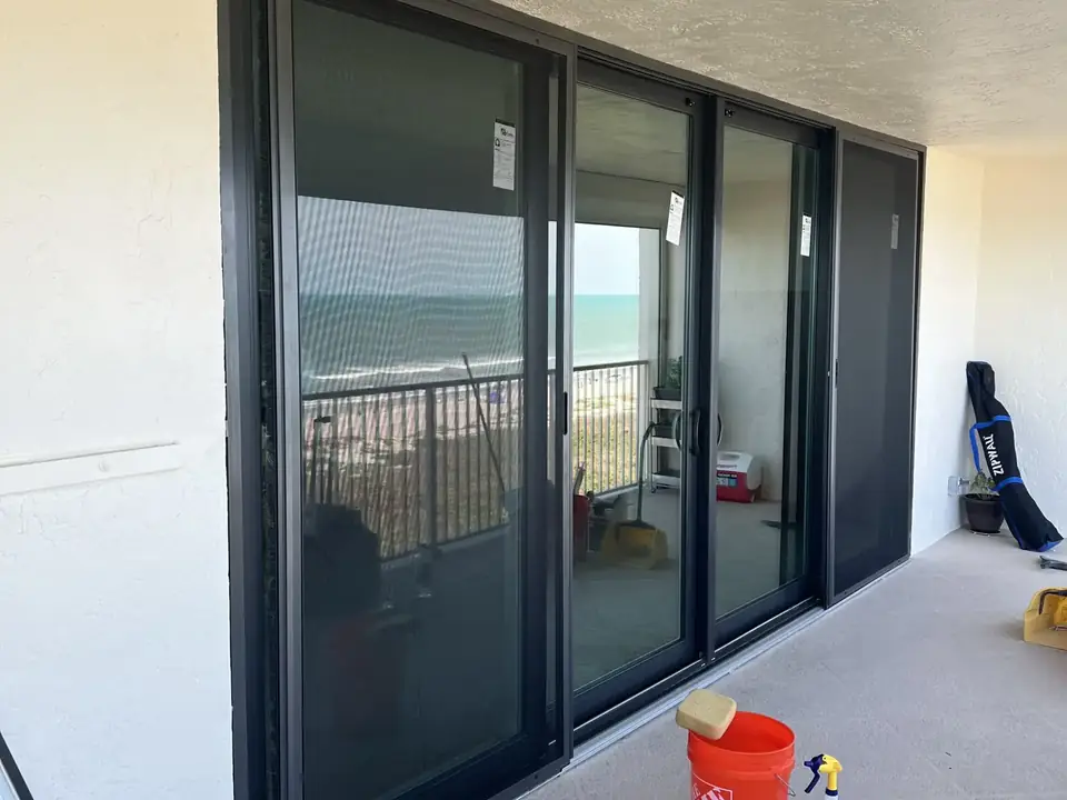 Floor-to-ceiling dark-frame impact sliding doors on an oceanfront condo balcony