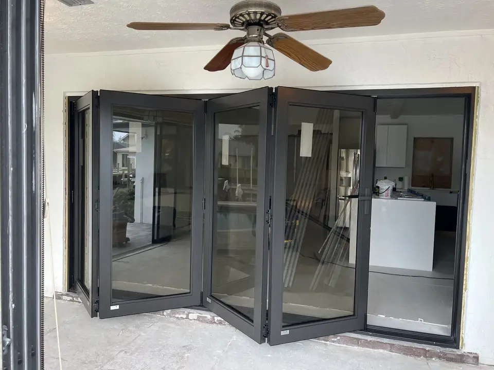 Black-frame folding impact glass doors opening a living room to the patio